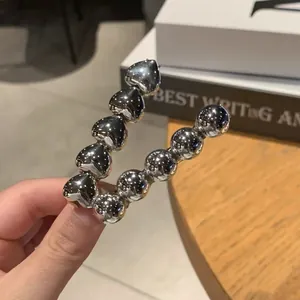 Minimalist silver heart and ball U-shaped hair clip shown on a warm aesthetic background
