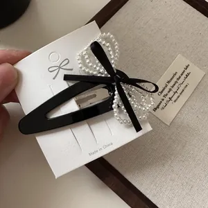 Detail of a black velvet bow hair clip with white faux pearls on a display card