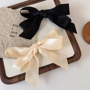 Elegantes Set aus Satin-Haarschleifen in Schwarz und Beige auf einem Holztablett
