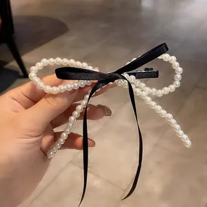 Detail showing pearl bow hair clip with elegant black satin ribbons and metallic grip