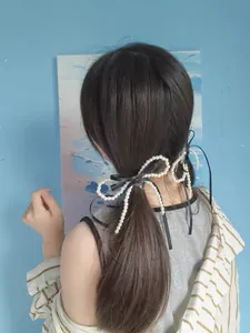 Detail of elegant pearl bow hair clip with black silk ribbon worn on a ponytail hair