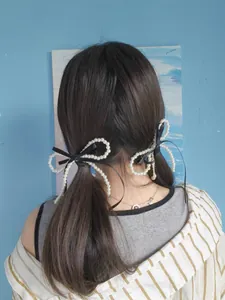 Detail showing two pearl bow hair clips with black ribbon worn on double ponytails
