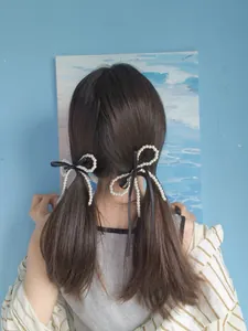 Close-up of dual pearl bow hair clips with black ribbons on a ponytail style
