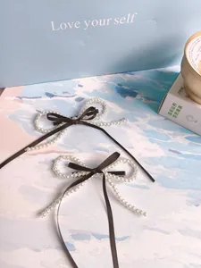 Detail of woven faux pearl bow hair clips with brown ribbon on a light blue gift box