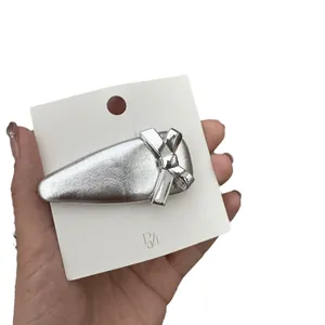 Barrette à cheveux argentée avec nœud et fini métallique sur carte blanche