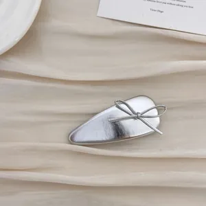 Close-up of a silver bow hair clip with sleek metallic finish on beige fabric background