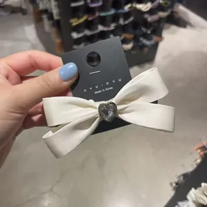 Detail shot of white satin bow hair clip with a clear heart crystal on display card