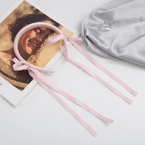 Detail view of pink satin headband with delicate long ribbons on white background