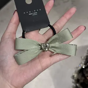 Dettaglio di elastico per capelli in raso verde salvia con cristallo a forma di cuore