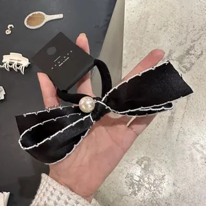 Elegant black satin bow hair tie with a central white pearl on a display card