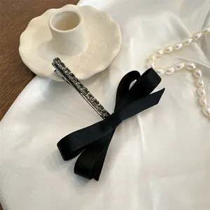 Elegante pasador de pelo vintage con lazo negro y diamantes sobre fondo de seda blanca