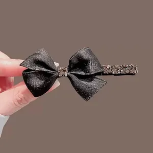 Barrette à cheveux nœud en satin noir ornée de strass brillants sur un fond marron sobre