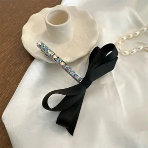 Elegante pasador de lazo negro con diamantes de imitación sobre fondo de seda blanca