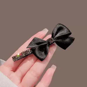 Pince à cheveux nœud noir élégante avec strass brillants et texture satinée sur fond brun