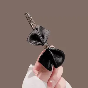 Détail d'une pince à cheveux nœud en satin noir avec des cristaux brillants sur base métal