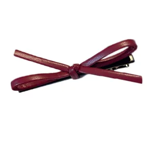 Elegant deep red leather bow hair clip with black metal fastener on white background