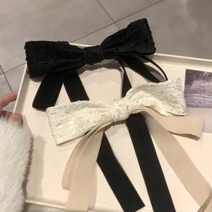 Elegant lace bow hair clip with long ribbons in black and beige displayed on a tray
