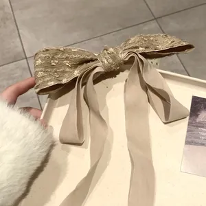 Detailed texture of a vintage bow hair clip with golden brocade and long cream ribbons
