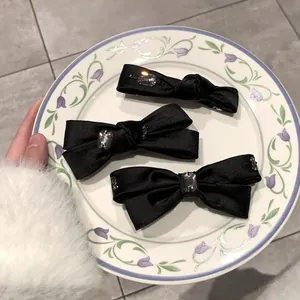 Dreiteiliges Set schwarzer Satin-Haarspangen mit Strassbesatz auf einem Keramikteller