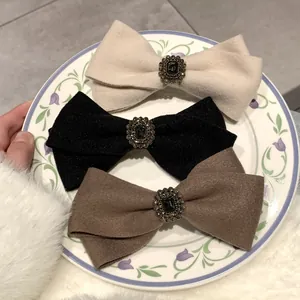 Detail of wool bow hair clips with vintage jewel center in cream, black, and brown