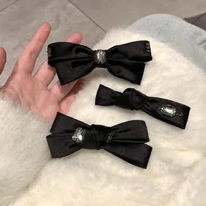 Detailansicht schwarzer Satin-Haarspangen mit Kristallakzenten auf weißem Plüsch