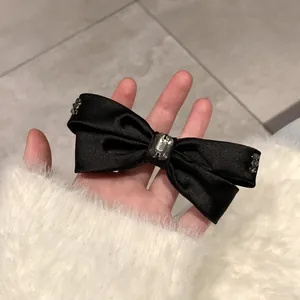 Detail einer schwarzen Satin-Haarschleife mit zentralem Kristall und Strasssteinen
