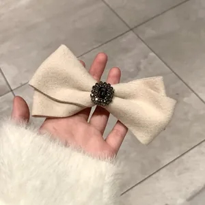Close-up of beige wool bow hair clip with central black gemstone and crystal trim