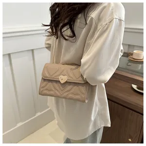Detail showing beige heart-quilted crossbody bag with a golden heart-shaped metal twist lock