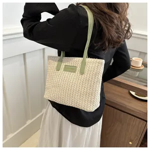 Detail of straw woven tote bag featuring green leather handles and fashion logo patch