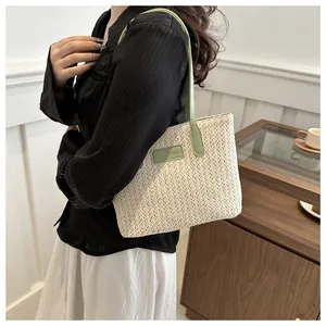 Detailed close-up of woven straw tote bag with green leather handle and fashion logo tag