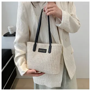 Detail of cream woven tote bag featuring black leather patch with gold text and thin straps