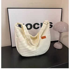 Close-up of beige corduroy dumpling bag featuring side pocket and sport leather label