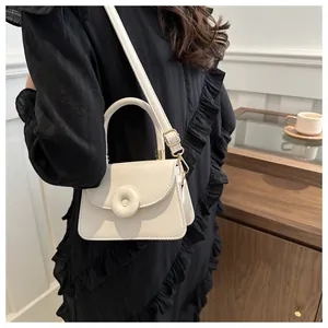 Close-up of a cream leather square handbag with golden buckle held by a model