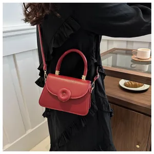 Detailed side view of a stylish red leather square handbag worn by a model in a cafe