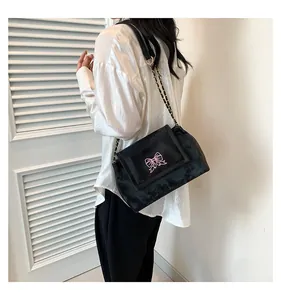 Détail du sac bandoulière en velours noir avec broderie papillon rose et chaîne métal