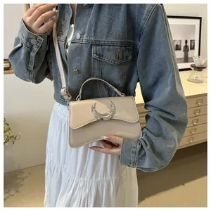 Détail d'un sac bandoulière minimaliste en cuir crème avec boucle lune argentée sur veste