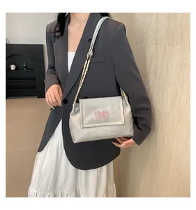 Détail du sac à bandoulière argenté avec broderie papillon rose et chaîne en métal