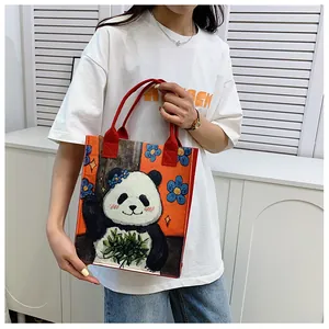 Detail view of felt panda tote bag with red handles held by a model in casual setting
