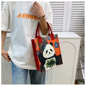Detail of felt panda tote bag with orange floral print and red handles on a white background