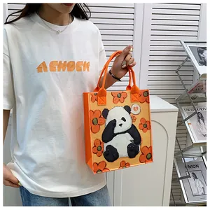 Detail of orange felt tote bag with panda floral print held by a model in a modern room