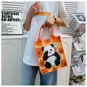 Close-up of orange felt tote bag featuring cartoon panda and flower graphics on a model