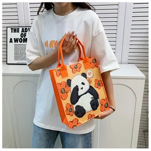 Detailed view of an orange felt tote bag with a panda and flower print held by a model