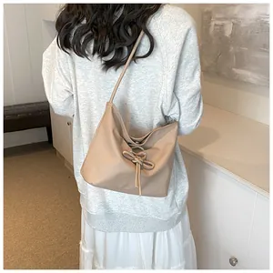 Detailed view of beige hobo bag with leather bow decoration on a model shoulder