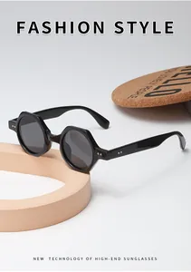 Détail de lunettes de soleil polygonales noires avec rivets argentés sur support beige