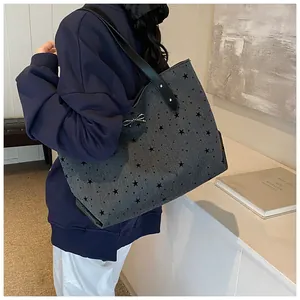Detail of grey star-print tote bag with black leather handles and silver bow pendant