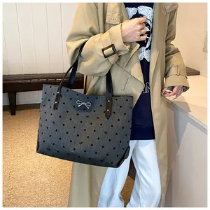 Detail of grey polka dot tote bag with metal bow pendant and black leather straps