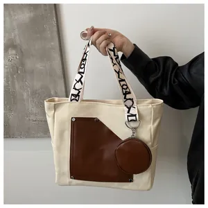 Handheld detail of large canvas tote bag with brown patchwork pocket and stylized straps.