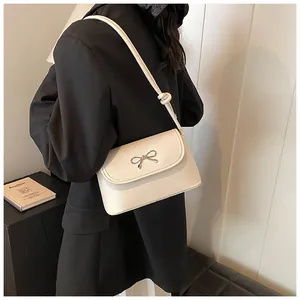 Detailed shot of chic cream shoulder bag with elegant silver bow accent, versatile design.