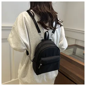 Modelo con una pequeña mochila negra de nailon impermeable y tirantes finos de tela