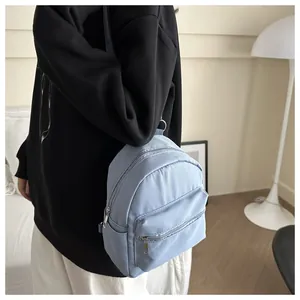 Vista trasera de una mini mochila azul claro con múltiples bolsillos con cremallera en modelo